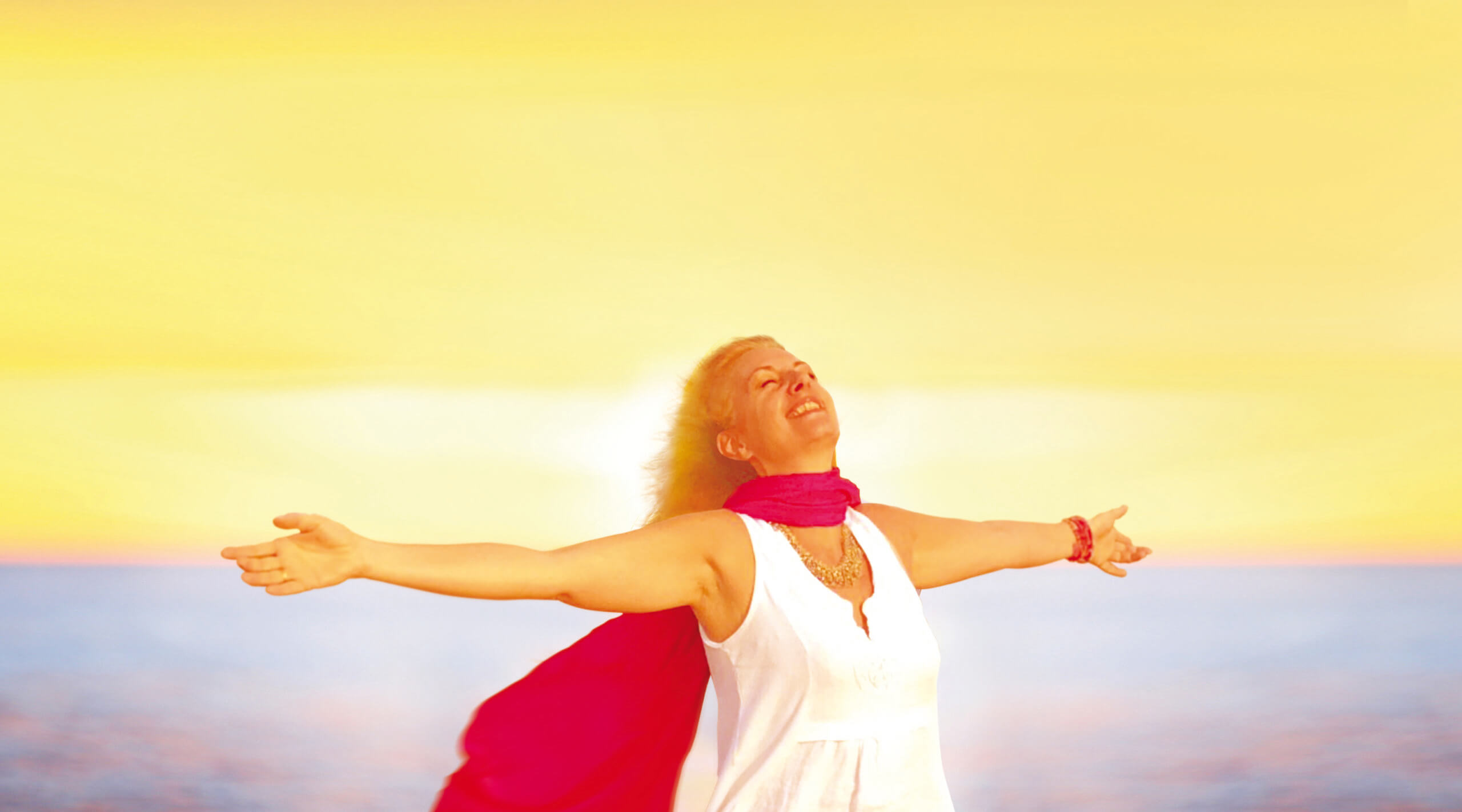 Enjoyment - free happy woman enjoying sunset. Beautiful woman in a white dress embracing the golden sunshine glow of sunset with her arms outspread and face raised to the sky enjoying peace and serenity of nature
